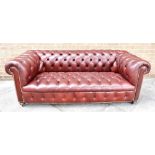 A BURGUNDY COLOURED LEATHER UPHOLSTERED CHESTERFIELD SOFA on turned wooden bun feet with casters,