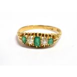 AN EMERALD AND DIAMOND FIVE STONE 18CT GOLD RING The boat shaped head carved claw set with three