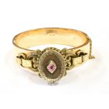 A LATE VICTORIAN BANGLE WITH LOCKET FRONT The oval hinged locket front set with a small ruby to