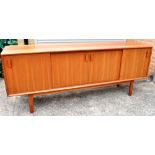 A 1960S TEAK SIDEBOARD fitted with four sliding doors enclosing drawers and shelves, 201cm long,