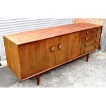 A 1960S SIDEBOARD with twin door cupboard flanked by four drawers, on tapering cylindrical supports,