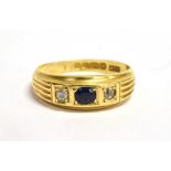 AN EDWARDIAN SAPPHIRE AND DIAMOND THREE STONE BAND RING The 18ct gold band carre set with a small