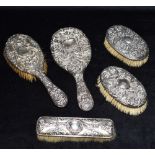 A SILVER FIVE PIECE BRUSH SET The embossed bird and mask pattern silver backed brush set