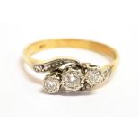 A SMALL DIAMOND THREE STONE 18CT GOLD RING the cross over design, illusion set with three small