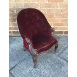 A MAHOGANY FRAMED CHILD'S BUTTON BACK ARMCHAIR upholstered in a dark red fabric and raised on