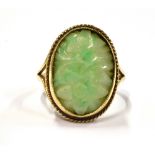 A 9CT GOLD JADE (?) STONE COCKTAIL RING With the oval floral carved stone measuring 2cm by 1.5 cm