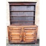 AN OAK DRESSER the upper section having a panelled back and a three shelf plate rack above a base of