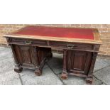 AN OAK PEDESTAL DESK having maroon leather top above two drawers and raised on two pedestals each