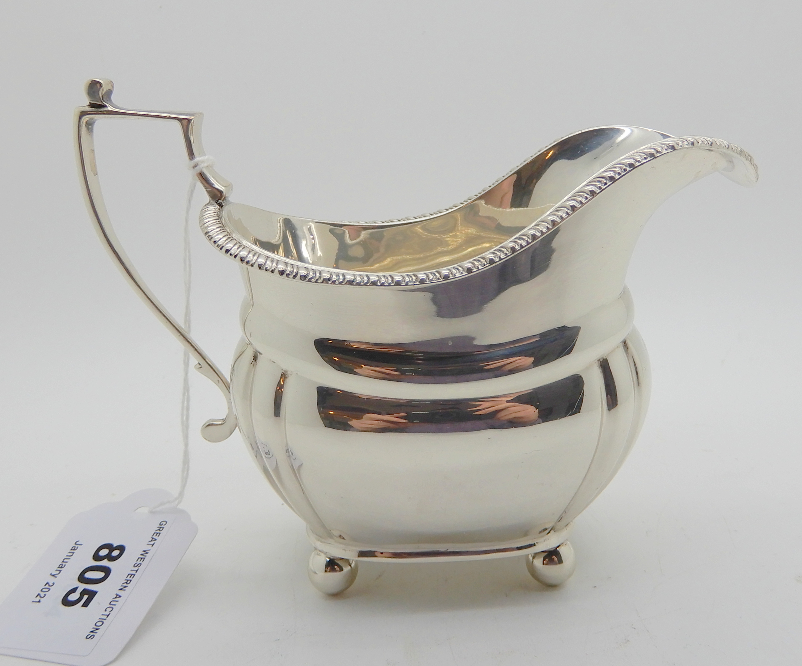 A silver cream jug, London 1924, of rounded rectangular form with lobed corners on four ball feet,