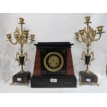 A French red marble and black slate mantle clock with a pair of candelabra garnitures, 43cm high