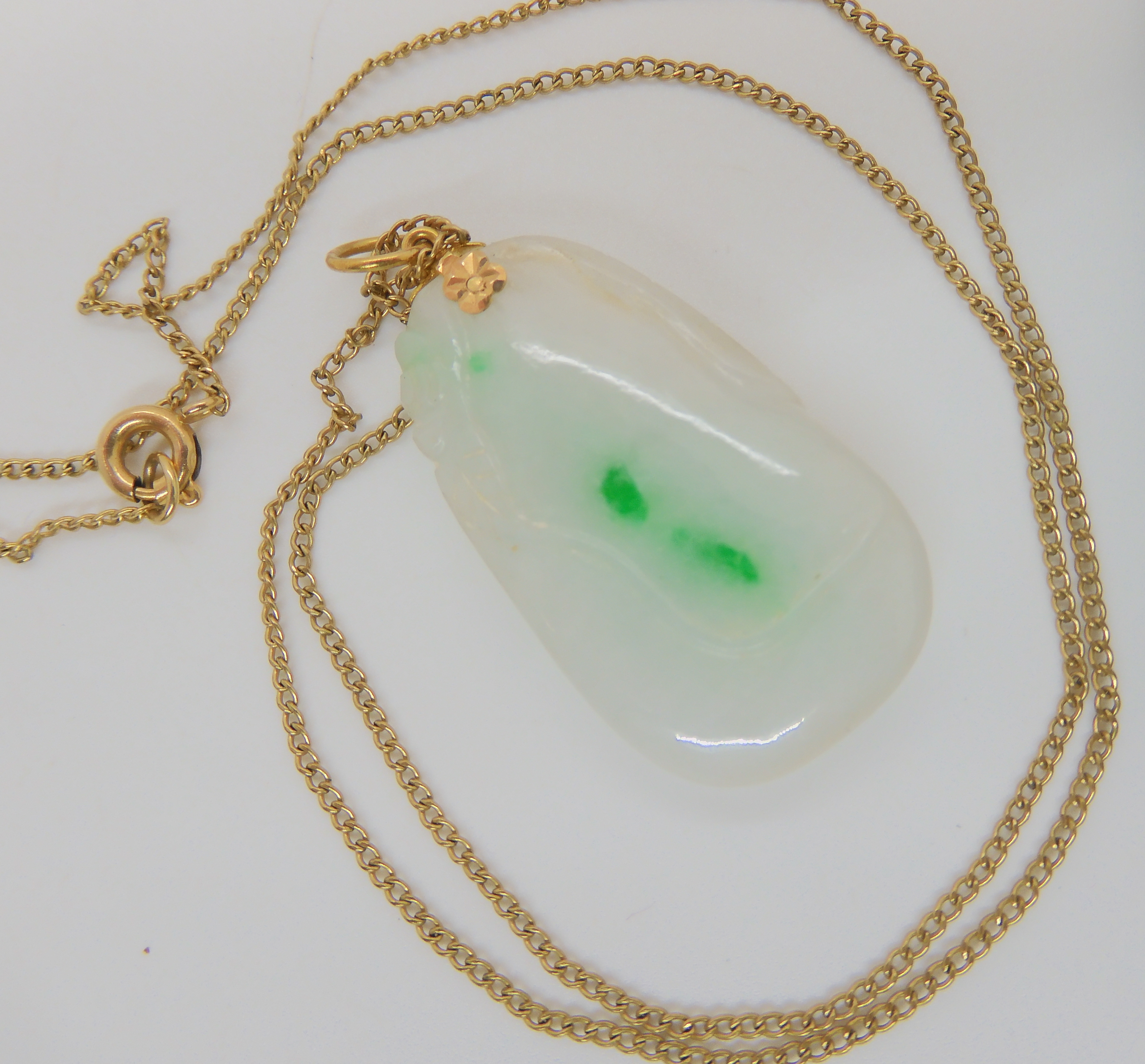 A white Chinese hardstone pendant carved with leaves with splashes of green, mounted in bright