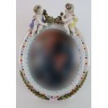 A CONTINENTAL MEISSEN STYLE OVAL DRESSING TABLE MIRROR mounted with cherubs holding a garland of
