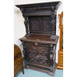 An oak cabinet with carved panel top on a base with single frieze drawer with mask handle and single