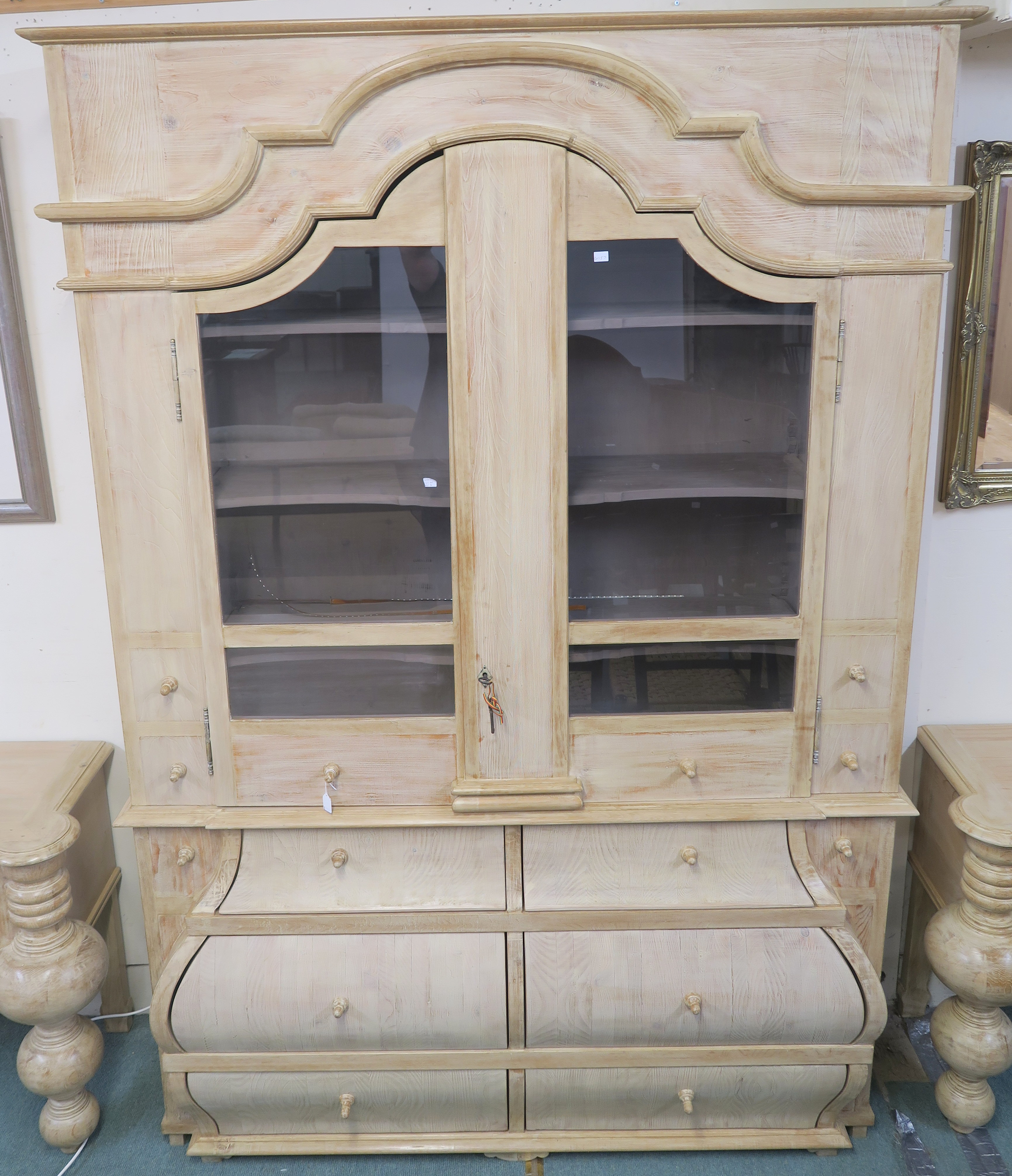 A modern limed pine display cabinet with shaped crown with two shaped glazed doors with shelves