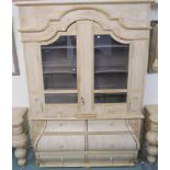 A modern limed pine display cabinet with shaped crown with two shaped glazed doors with shelves