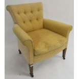 A yellow button back upholstered armchair with square tapering legs on ceramic castors, 84cm high