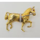 A 14K YELLOW GOLD HORSE BROOCH with a diamond set bridle and band around the stomach with a ruby set
