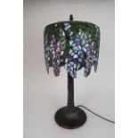 A LEADED AND STAINED GLASS TABLE LAMP the shade decorated as wisteria flowers, above a metal tree