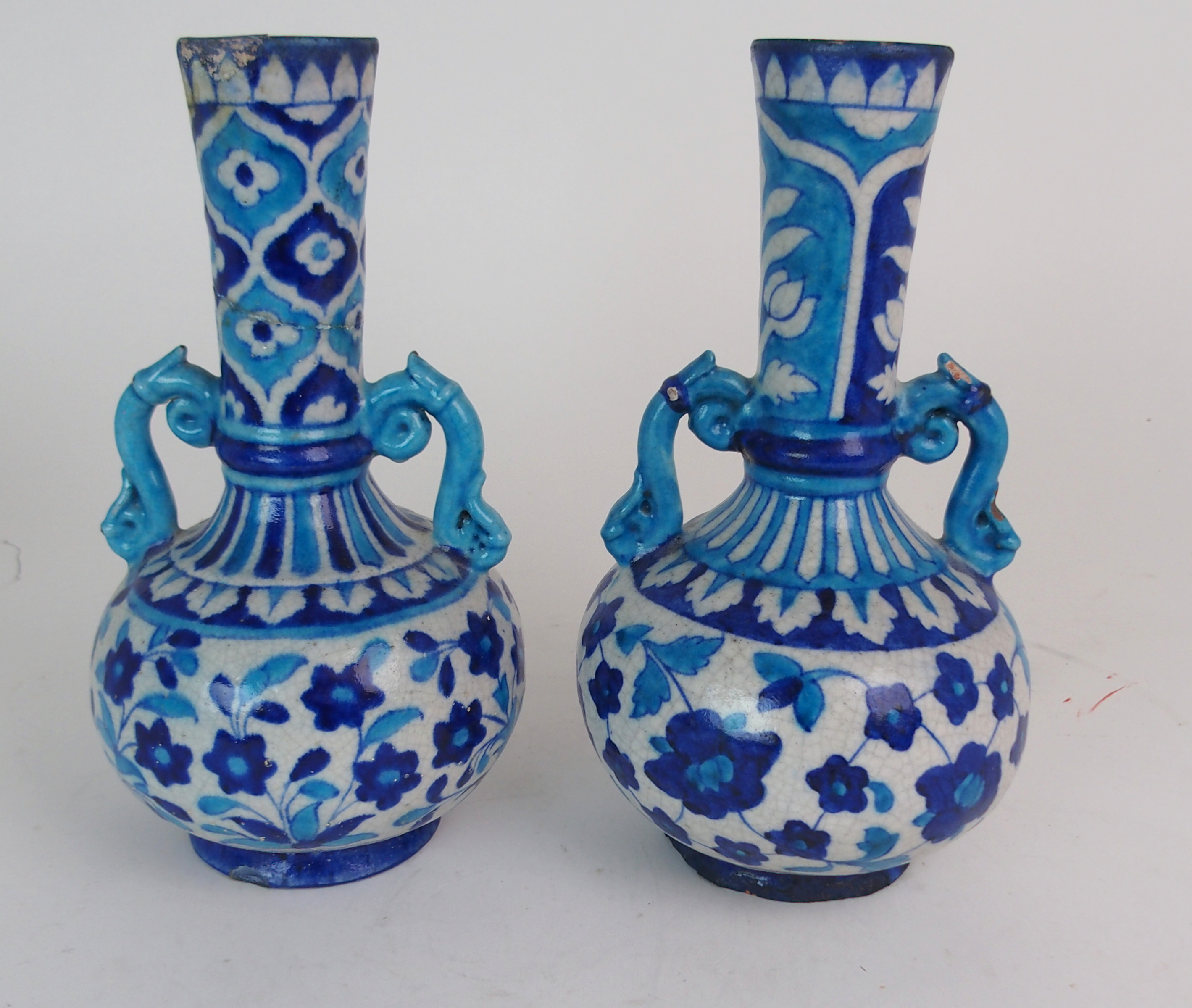 A PAIR OF PERSIAN POTTERY BLUE AND WHITE TWO HANDLED VASES painted with flowers and foliage, with