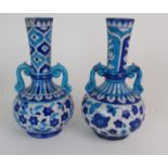 A PAIR OF PERSIAN POTTERY BLUE AND WHITE TWO HANDLED VASES painted with flowers and foliage, with