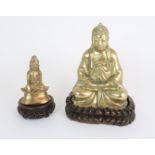 AN ASIAN BRASS MODEL OF BUDDHA seated in the lotus position and with carved wood base, 24.5cm