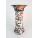 A JAPANESE IMARI FLARED CYLINDRICAL VASE painted with a building on stilts amongst flowering