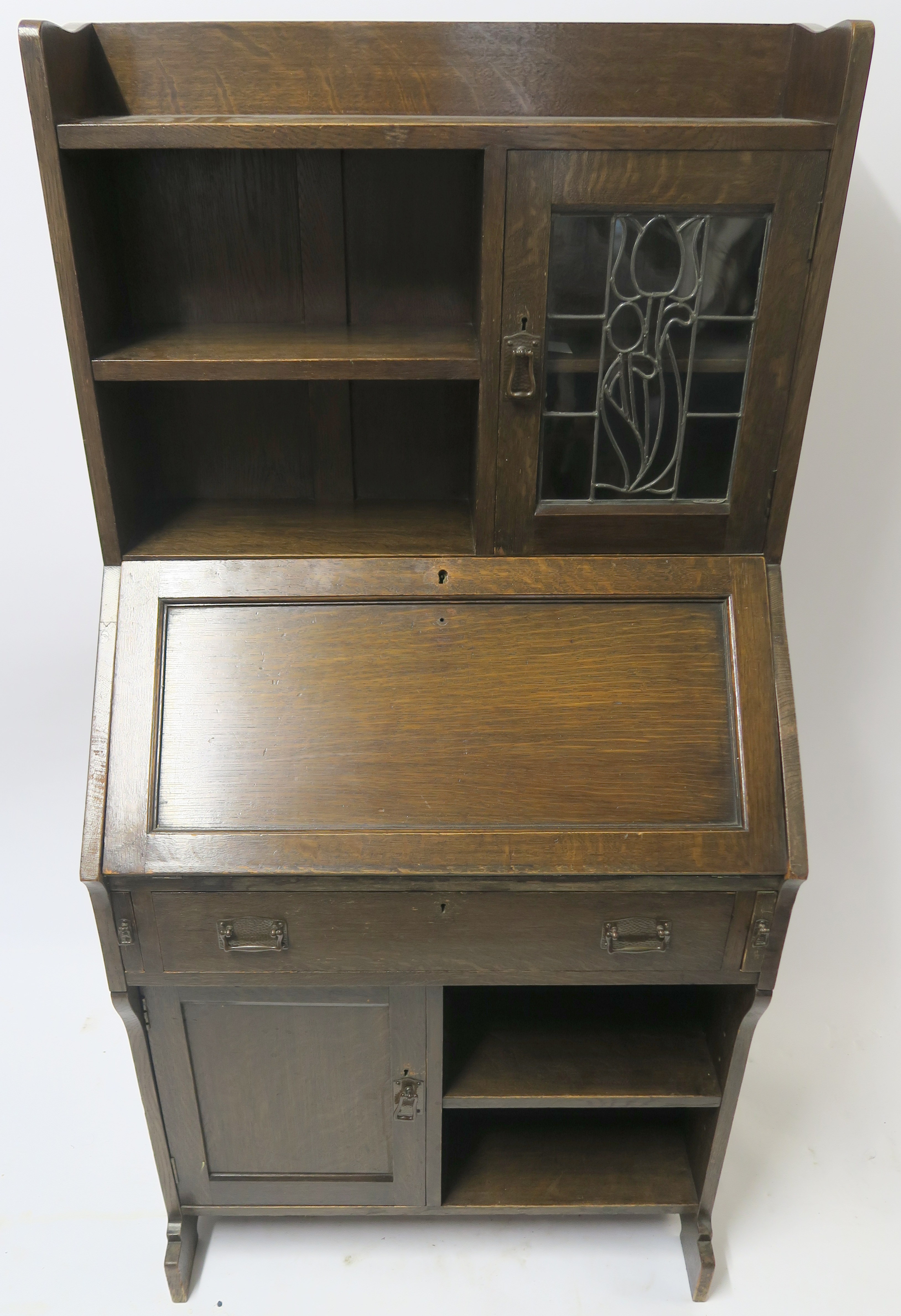 AN ARTS AND CRAFTS OAK WRITING DESK with a stained and leaded glass door and open shelves above a