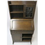AN ARTS AND CRAFTS OAK WRITING DESK with a stained and leaded glass door and open shelves above a