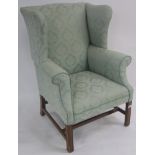 A Georgian style wingback armchair with green upholstery with mahogany square legs and an H