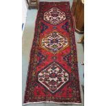 A red ground eastern runner with three medallions and multi colour borders, 313cm long x 114cm