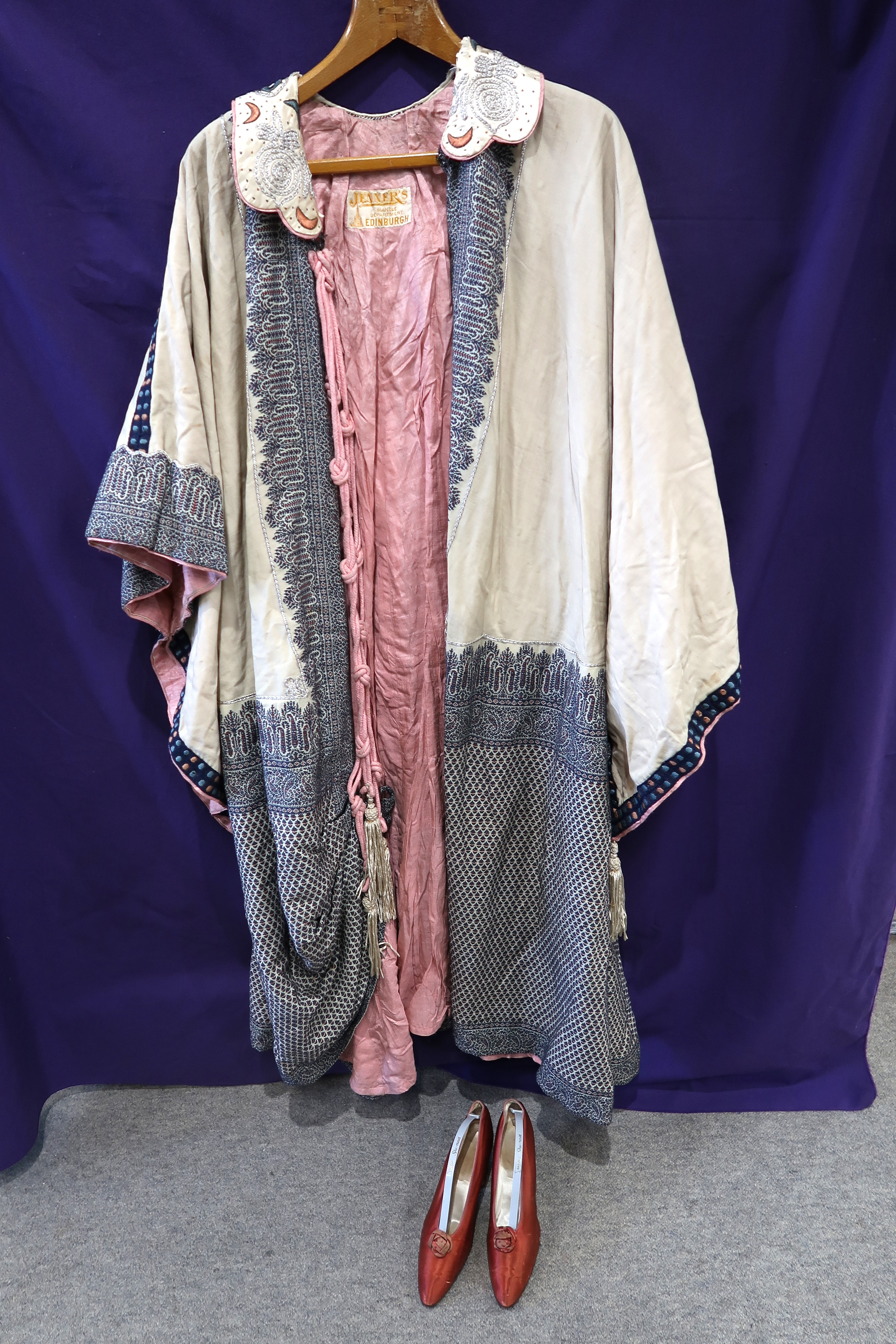 A cream ground embroidered Bedouin cloak with pink rope tassel fastenings and a pair of 1920s ruby