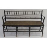A WILLIAM MORRIS SUSSEX EBONISED BENCH the back set with turned rails above a rush seat and on eight