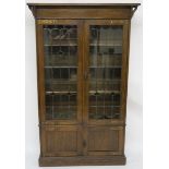AN ARTS AND CRAFTS OAK BOOKCASE with a pair of stained and leaded glass doors enclosing shelves,