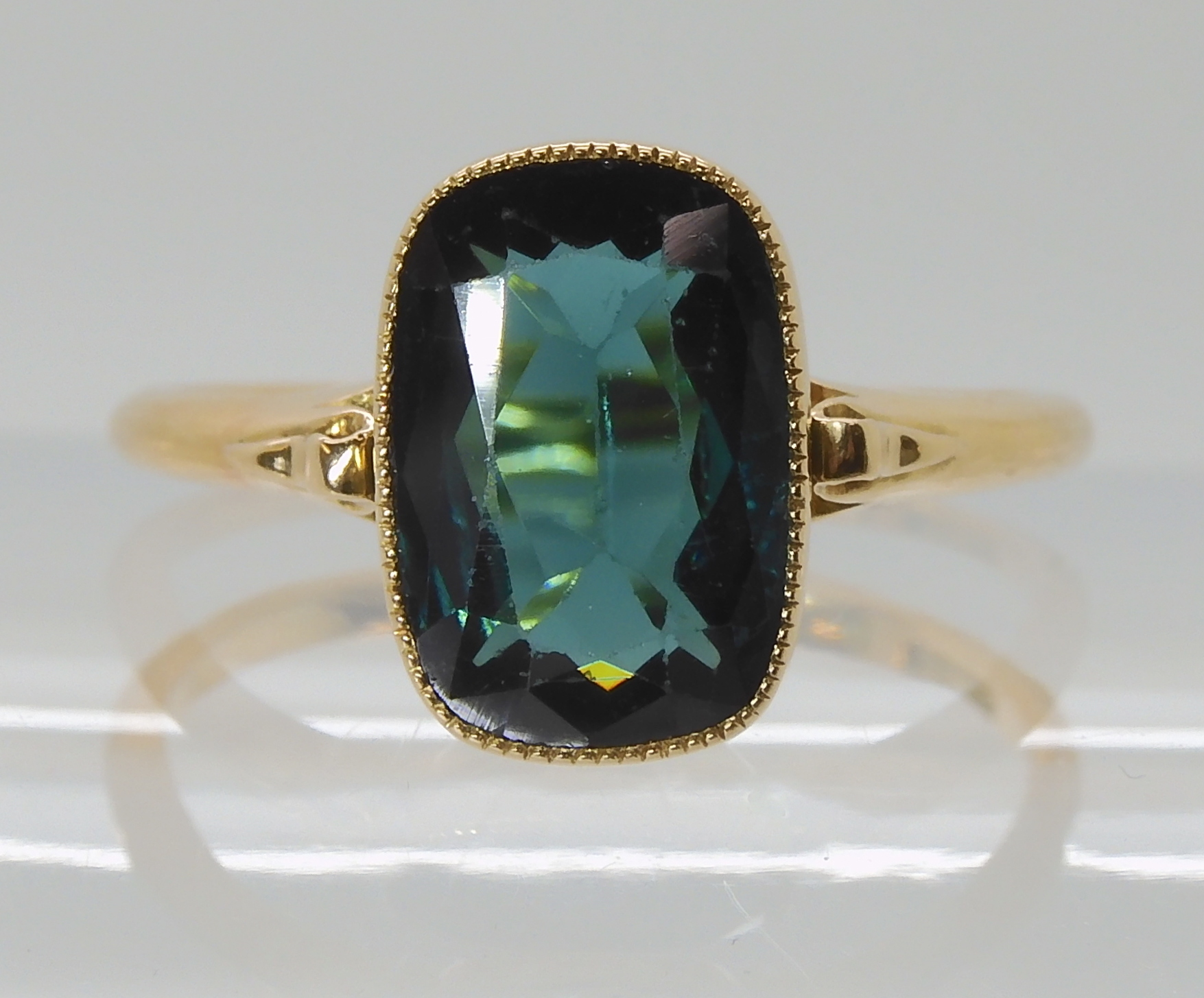 A TEAL COLOURED TOURMALINE RING mounted in bright yellow metal, with decorative scroll shoulders,