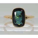 A TEAL COLOURED TOURMALINE RING mounted in bright yellow metal, with decorative scroll shoulders,