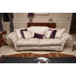 A contemporary scroll-arm three-seater size sofa, the cream fabric with couched silvered thread