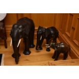 A contemporary leather 'family' of three elephants, naturalistically modelled with simulated-ivory