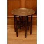 A Middle Eastern folding coffee table, early 20th century, the brass tray top with embossed