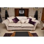 A contemporary scroll-arm three-seater size sofa, the cream fabric with couched silvered thread