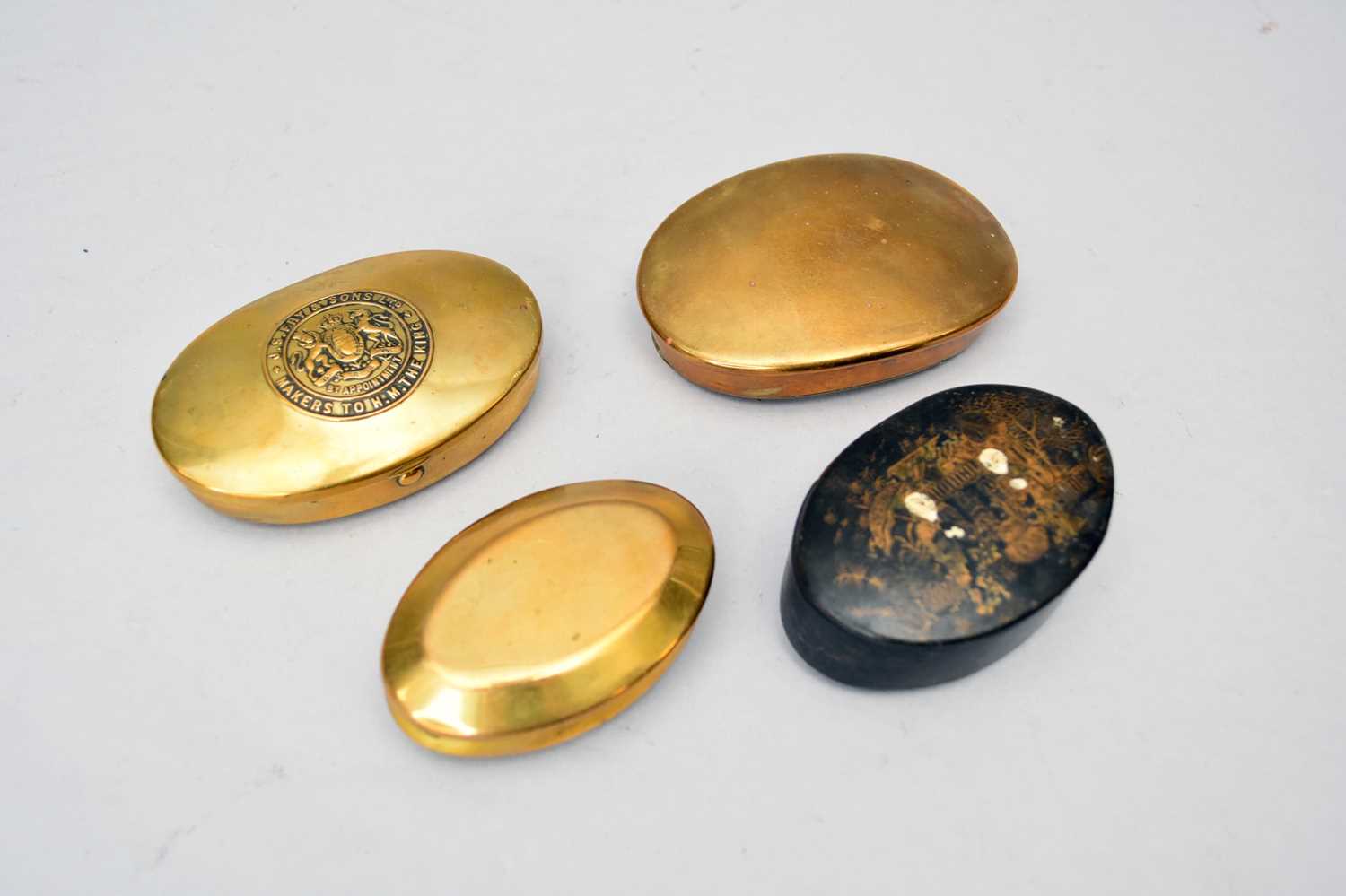Four oval snuff boxes comprising a papier-mache example, a brass miner's tobacco pouch, a J.S