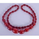 A CHERRY AMBER TYPE BEAD NECKLACE. 56 grams. 68 cm long, largest bead 2.5 cm wide.