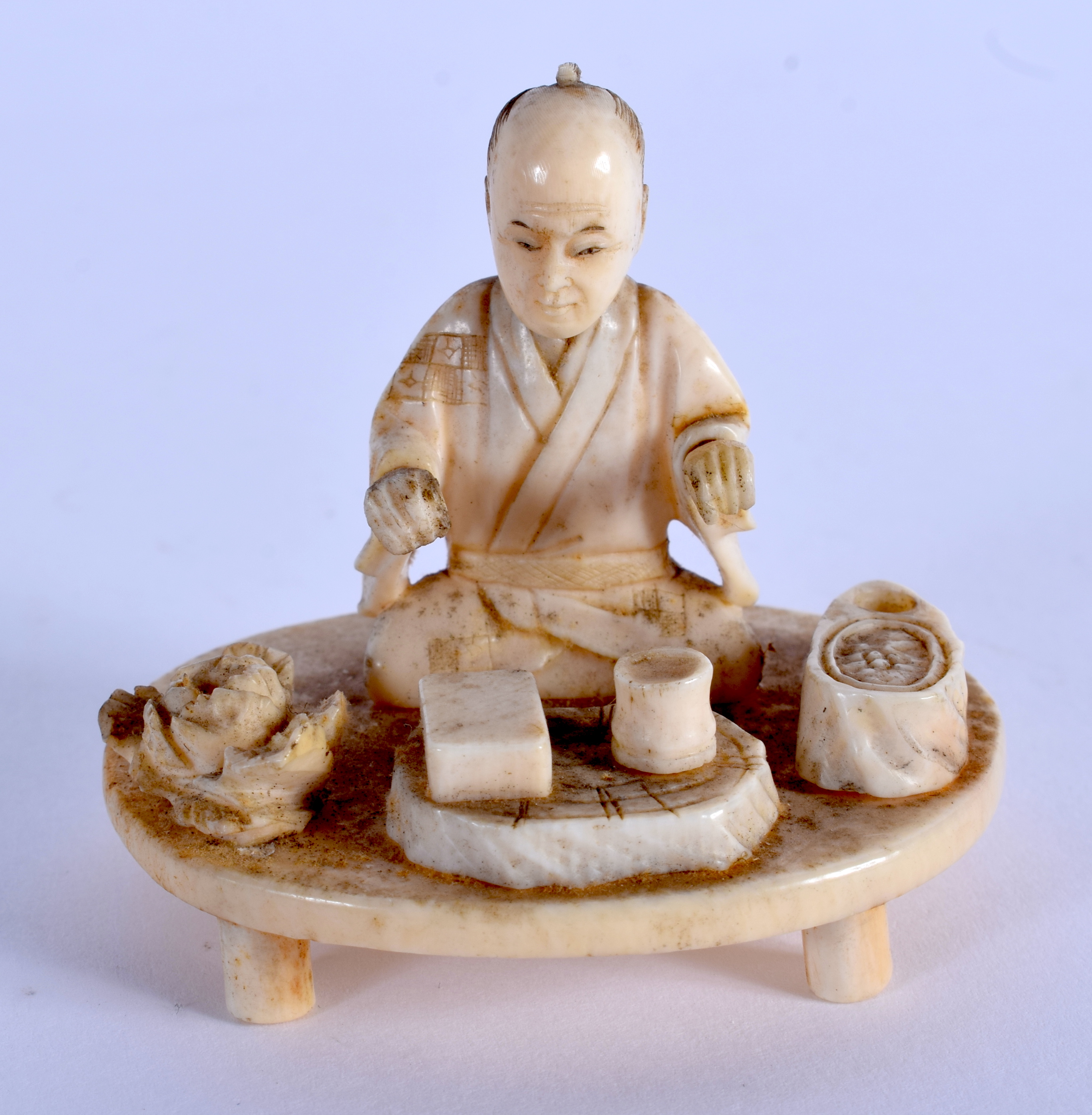 A 19TH CENTURY JAPANESE MEIJI PERIOD CARVED IVORY OKIMONO modelled as a male on a table. 5.5 cm x 5