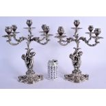A LOVELY PAIR OF CONTINENTAL SILVER CANDLEABRA modelled two cherubs holding aloft floral capped scon