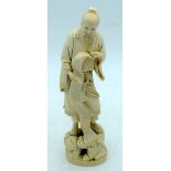 A 19TH CENTURY JAPANESE MEIJI PERIOD CARVED IVORY OKIMONO modelled holding a standing scroll upon a