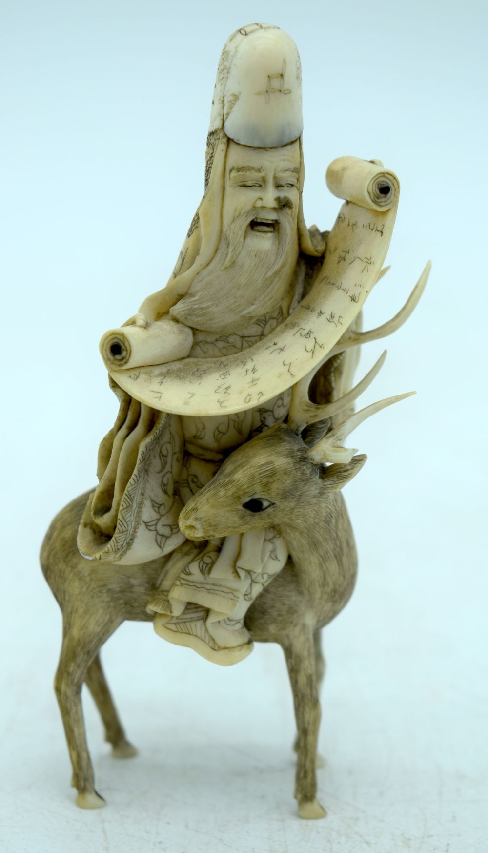 A 19TH CENTURY JAPANESE MEIJI PERIOD CARVED IVORY OKIMONO modelled holding a scroll upon a deer. 10