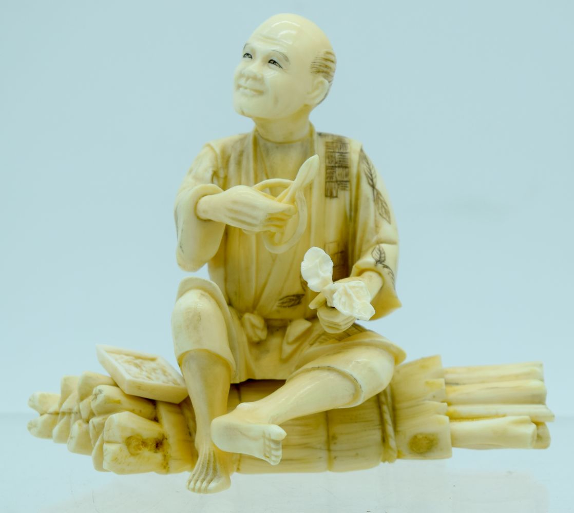 A 19TH CENTURY JAPANESE MEIJI PERIOD CARVED IVORY OKIMONO modelled as a male upon logs holding veget