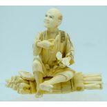 A 19TH CENTURY JAPANESE MEIJI PERIOD CARVED IVORY OKIMONO modelled as a male upon logs holding veget