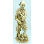 A 19TH CENTURY JAPANESE MEIJI PERIOD CARVED IVORY OKIMONO modelled standing upon a naturalistic outc