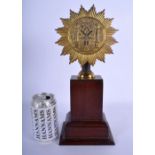 AN ANTIQUE MASONIC BRASS STANDARD upon an oak plinth. 33 cm x 8 cm.