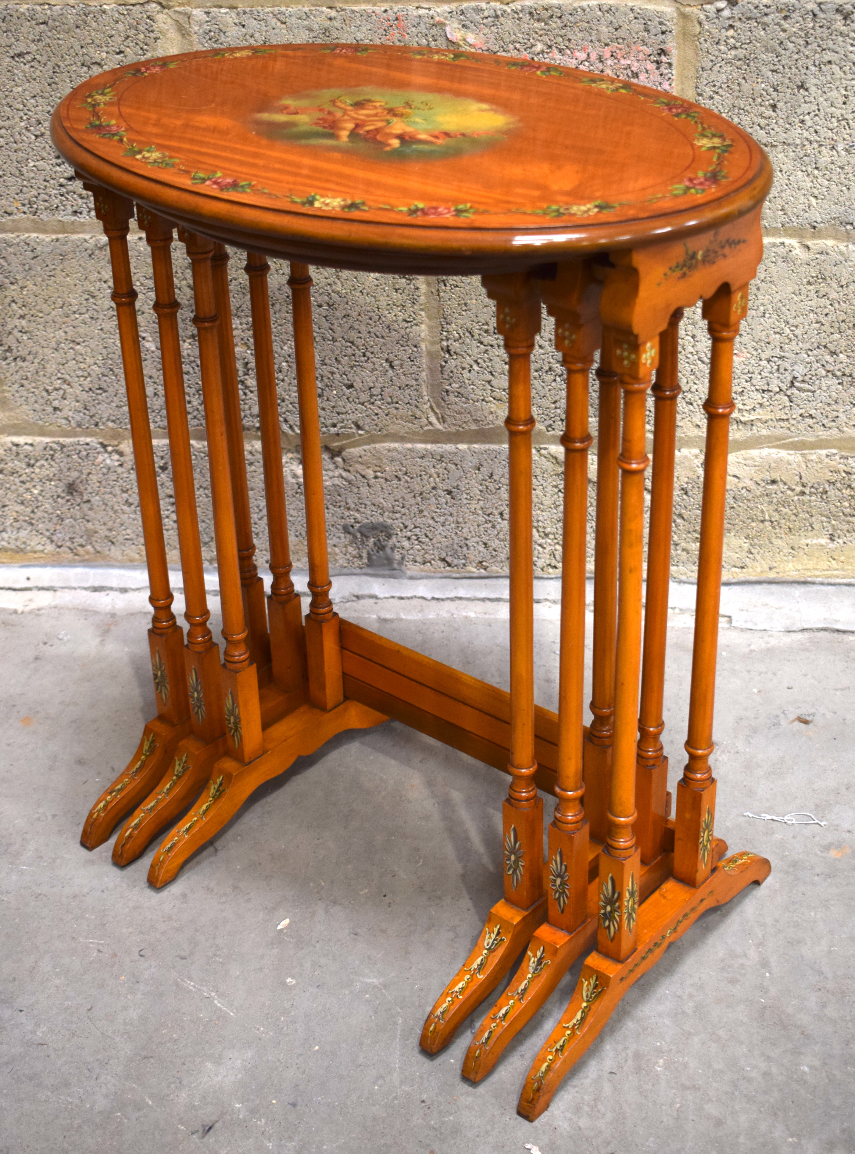 A NEST OF THREE EDWARDIAN PAINTED SATINWOOD TABLES decorated with putti in flight. Largest 57 cm x 6